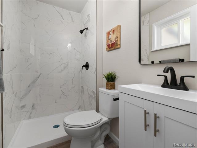 Bathroom with a marble-look walk-in shower, toilet, and white vanity with black faucet.