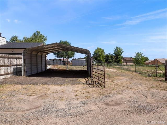 Yard with a metal-sided covered carport, gravel, and fencing.