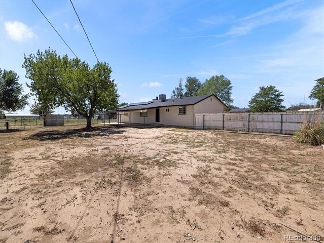 Single-story home behind a fenced dirt yard, with a mature tree in the foreground.
