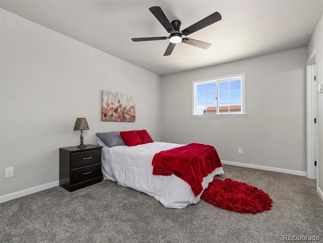 Staged bedroom with a white bed, red accents, gray carpet, and a ceiling fan.