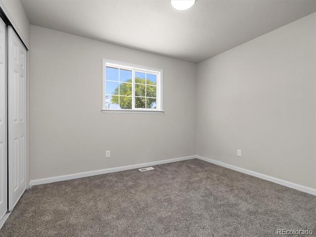 Empty carpeted bedroom with a window and sliding closet doors.