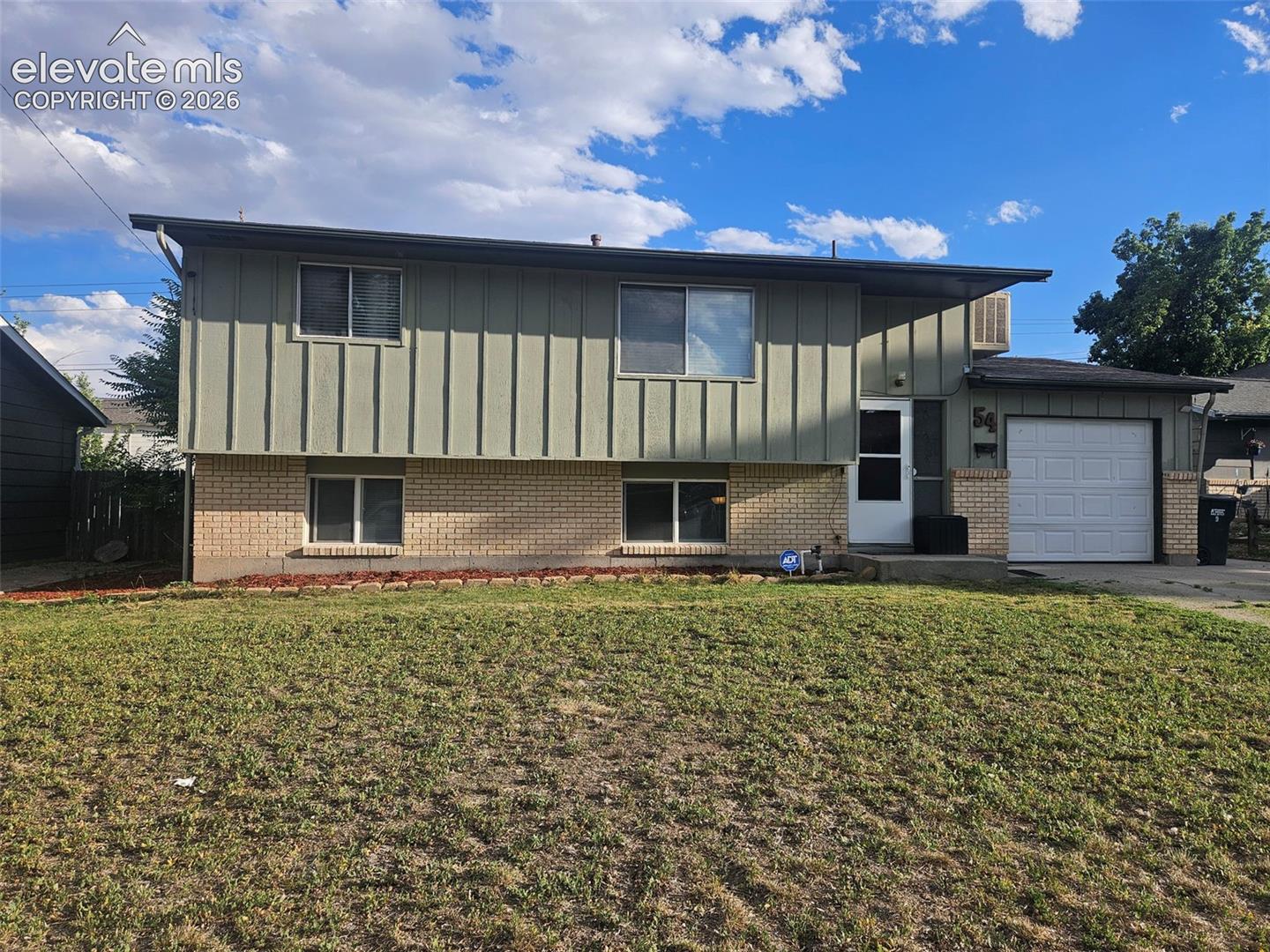 Split-level home with green siding, a brick lower facade, and an attached garage.