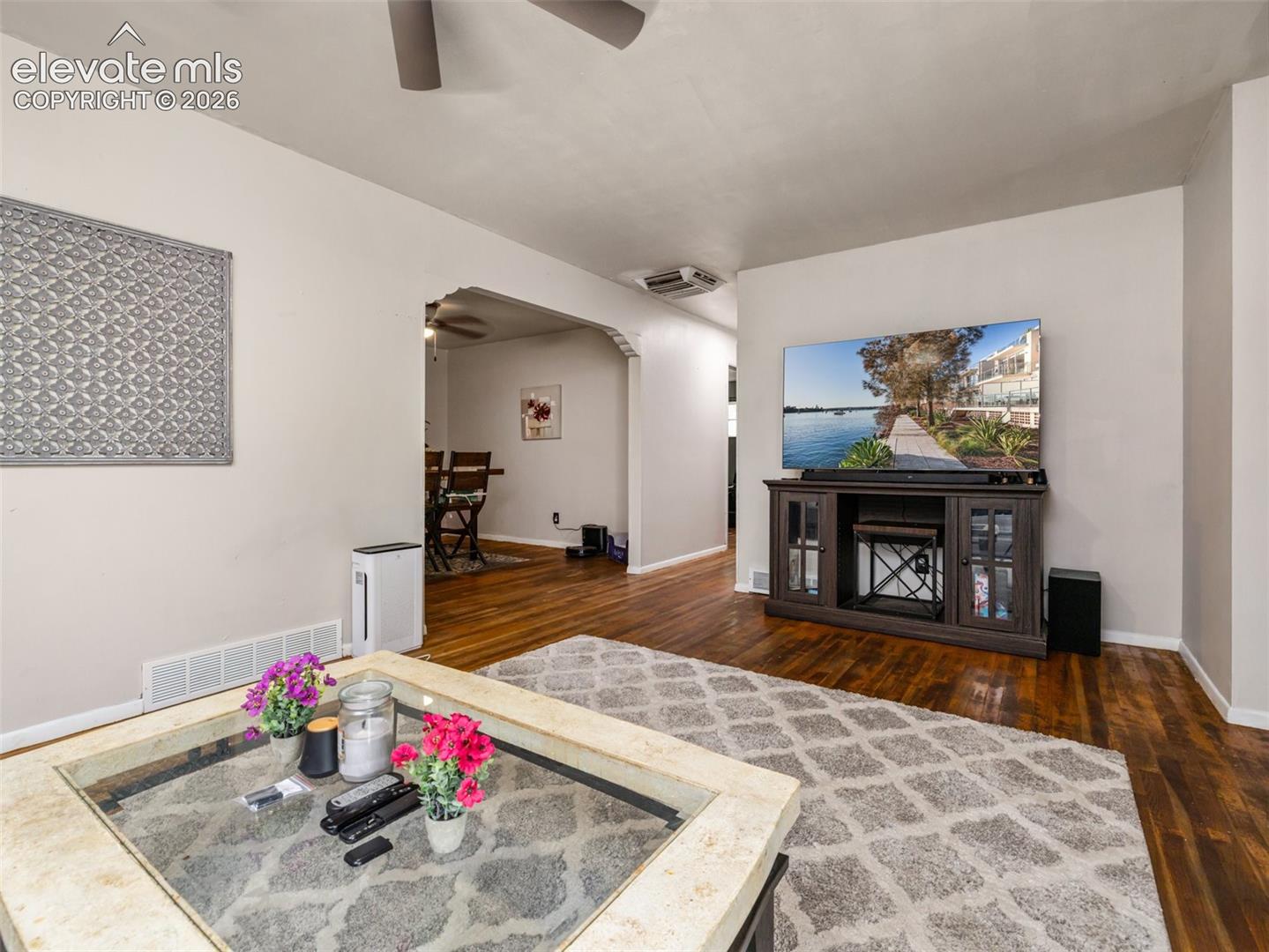 Living room with hardwood floors, patterned rug, glass-top coffee table, and TV console.
