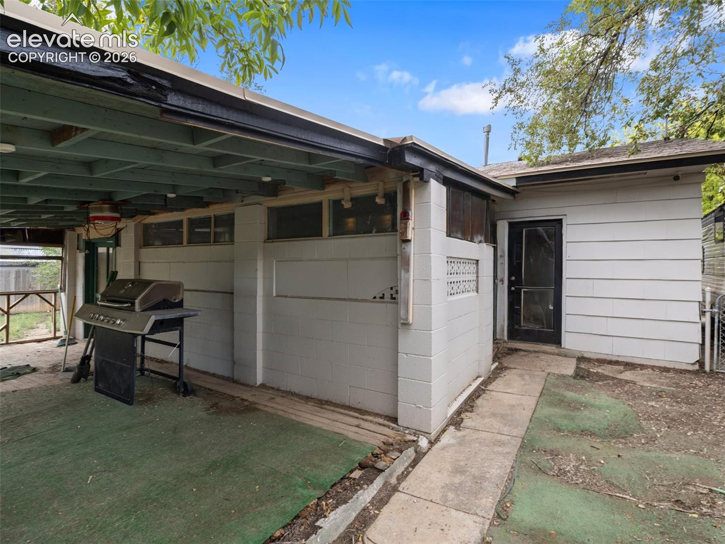 Covered patio with a barbecue grill, green flooring, and a screen door.