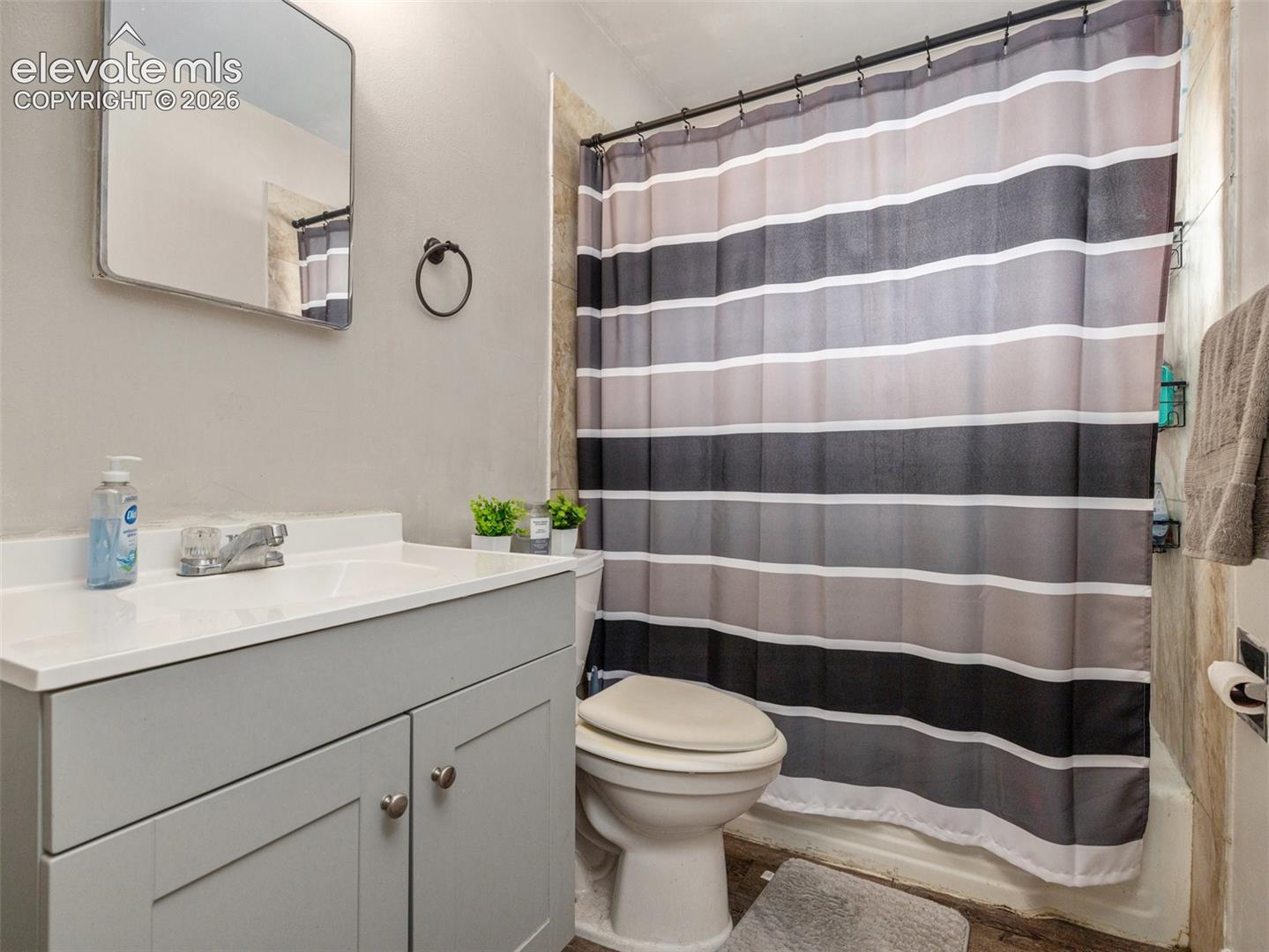 Bathroom with a white vanity, toilet, and gray striped shower curtain.