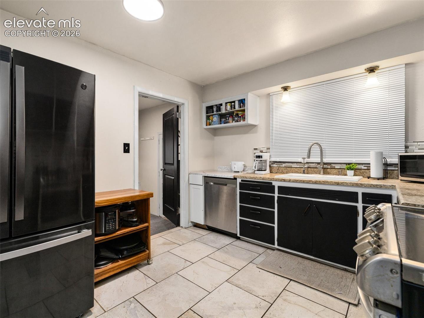 Kitchen with black cabinets, stainless steel appliances, and a large window above the sink.