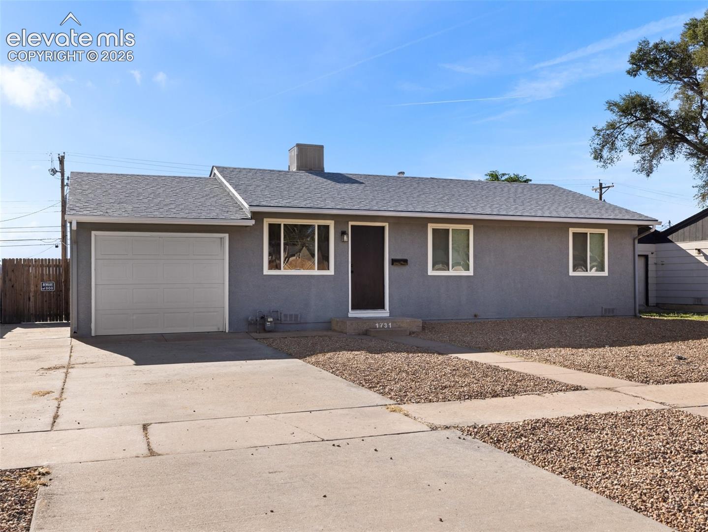 Gray single-story home with an attached garage, concrete driveway, and gravel landscaping.