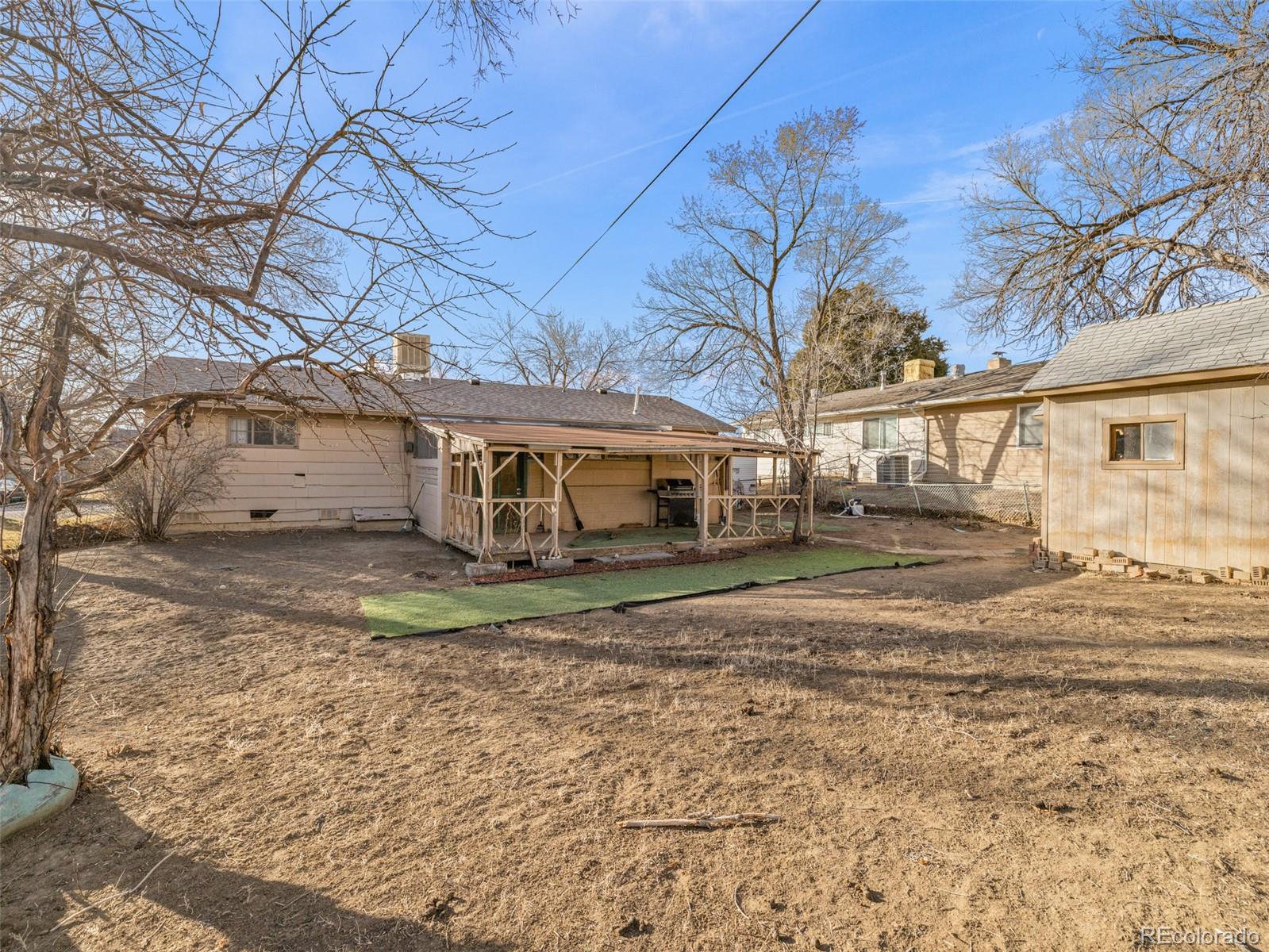 Home’s backyard with a covered patio, outdoor grill, shed, and patch of artificial turf.