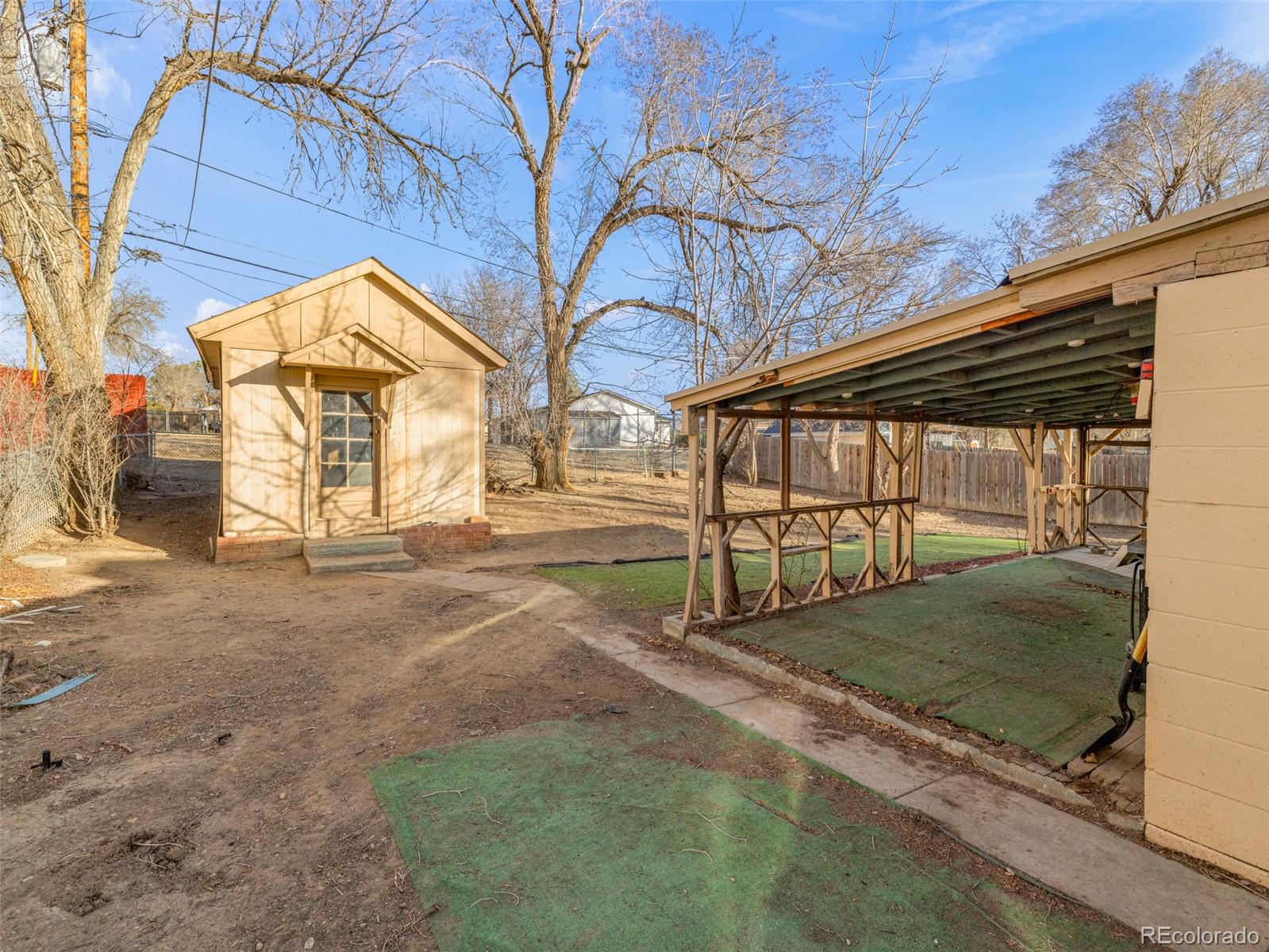 Backyard with a tan storage shed, covered outdoor area, and concrete path.