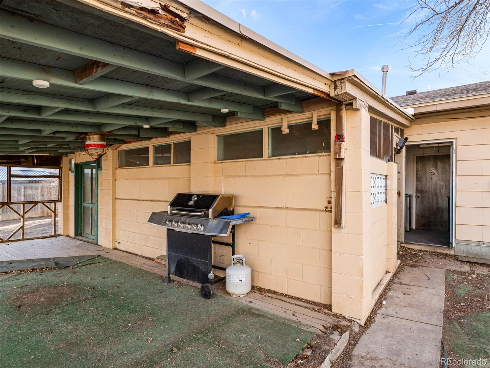Covered patio beside a beige house, with exposed beams and a gas grill.
