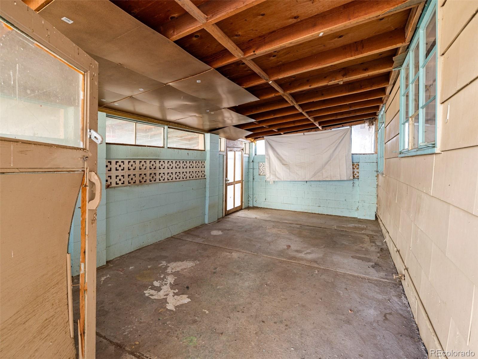 Empty garage with exposed wooden ceiling joists, blue block walls, and a worn concrete floor.