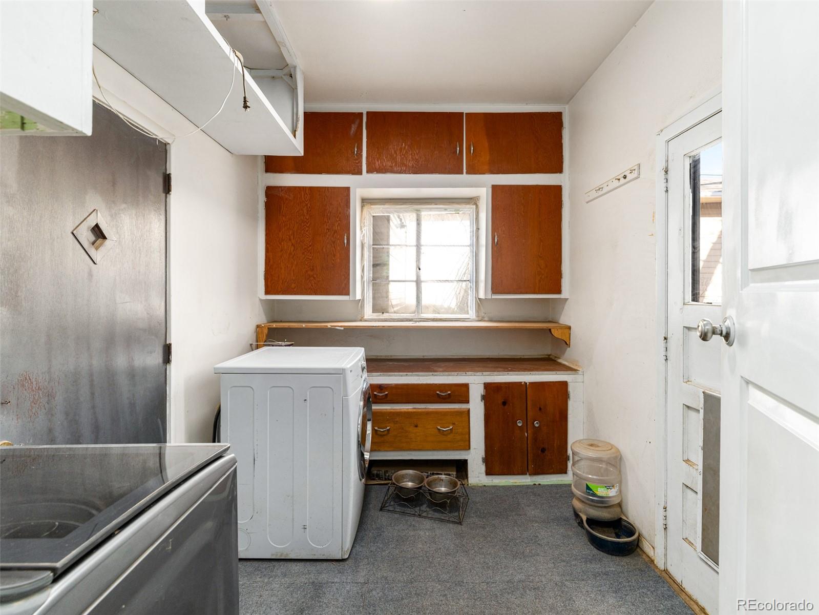 Laundry room with a white washer, wood cabinets, a window, and pet bowls.