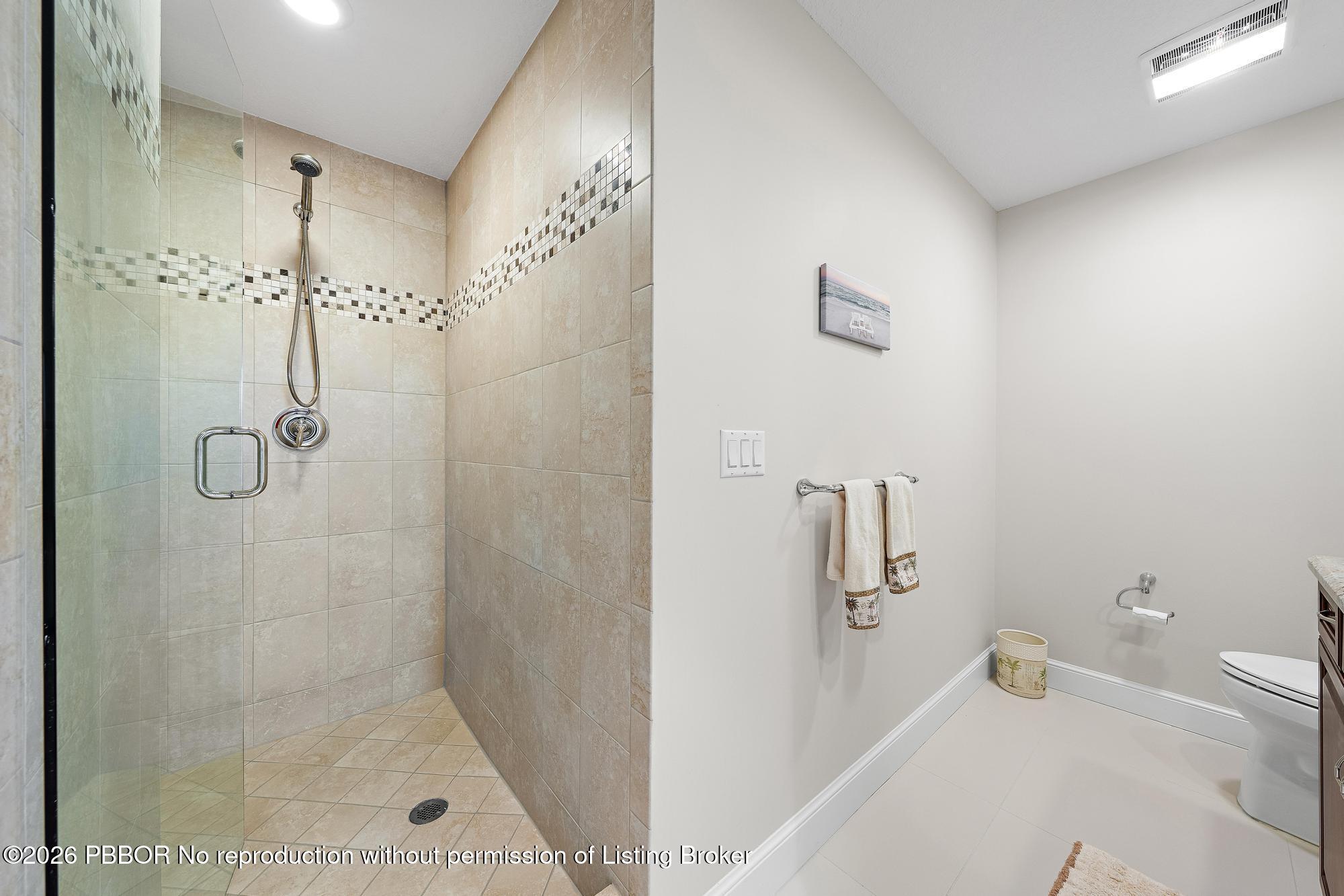Bathroom with a glass-enclosed walk-in shower tiled in beige with a decorative mosaic band.
