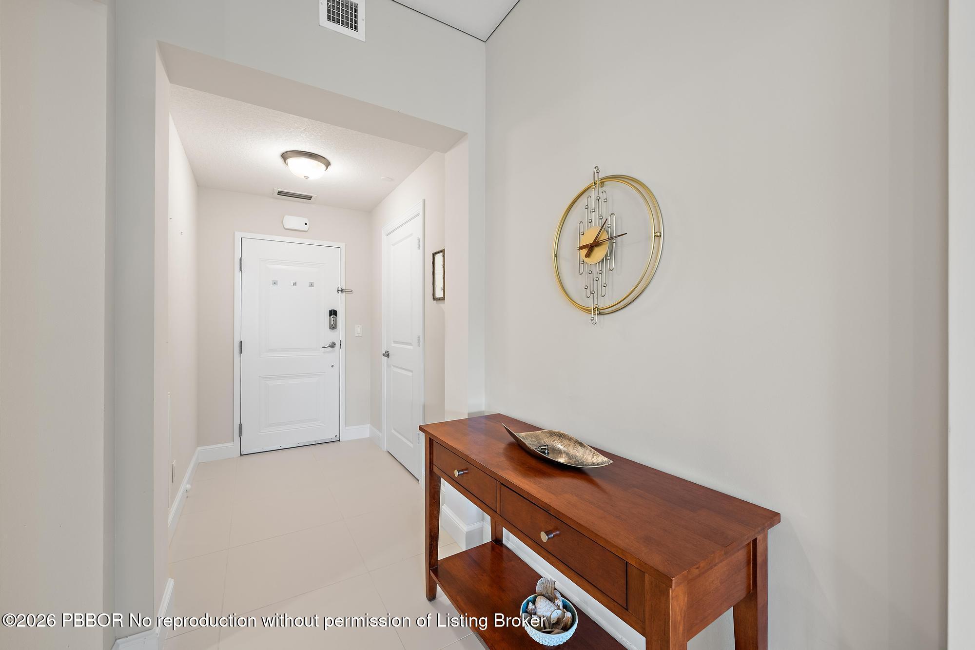 Entry foyer with a tiled floor, wood console table, and gold wall clock.