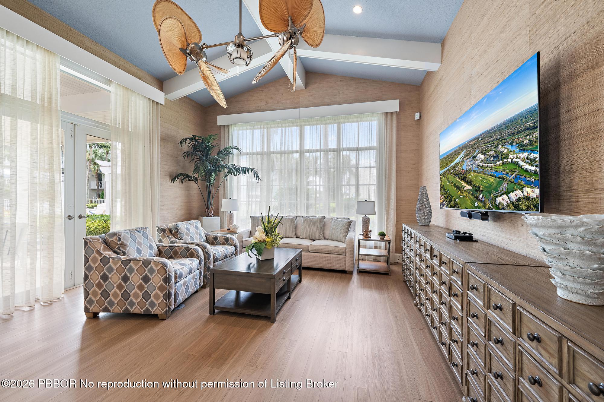 Furnished living room with a vaulted ceiling, patterned armchairs, and a large wall-mounted television.
