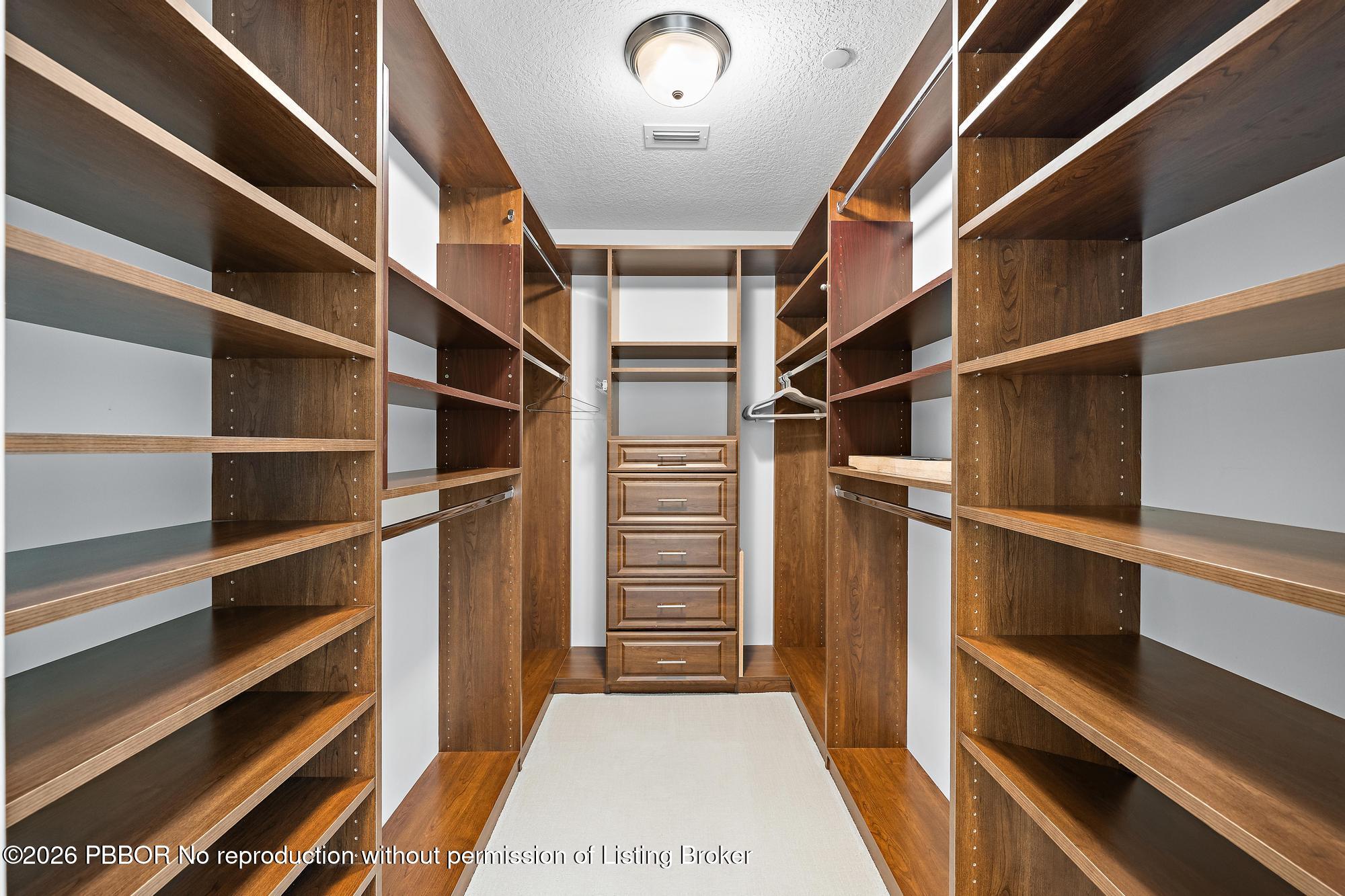 Walk-in closet with dark wood shelving, hanging sections, and a central stack of drawers.