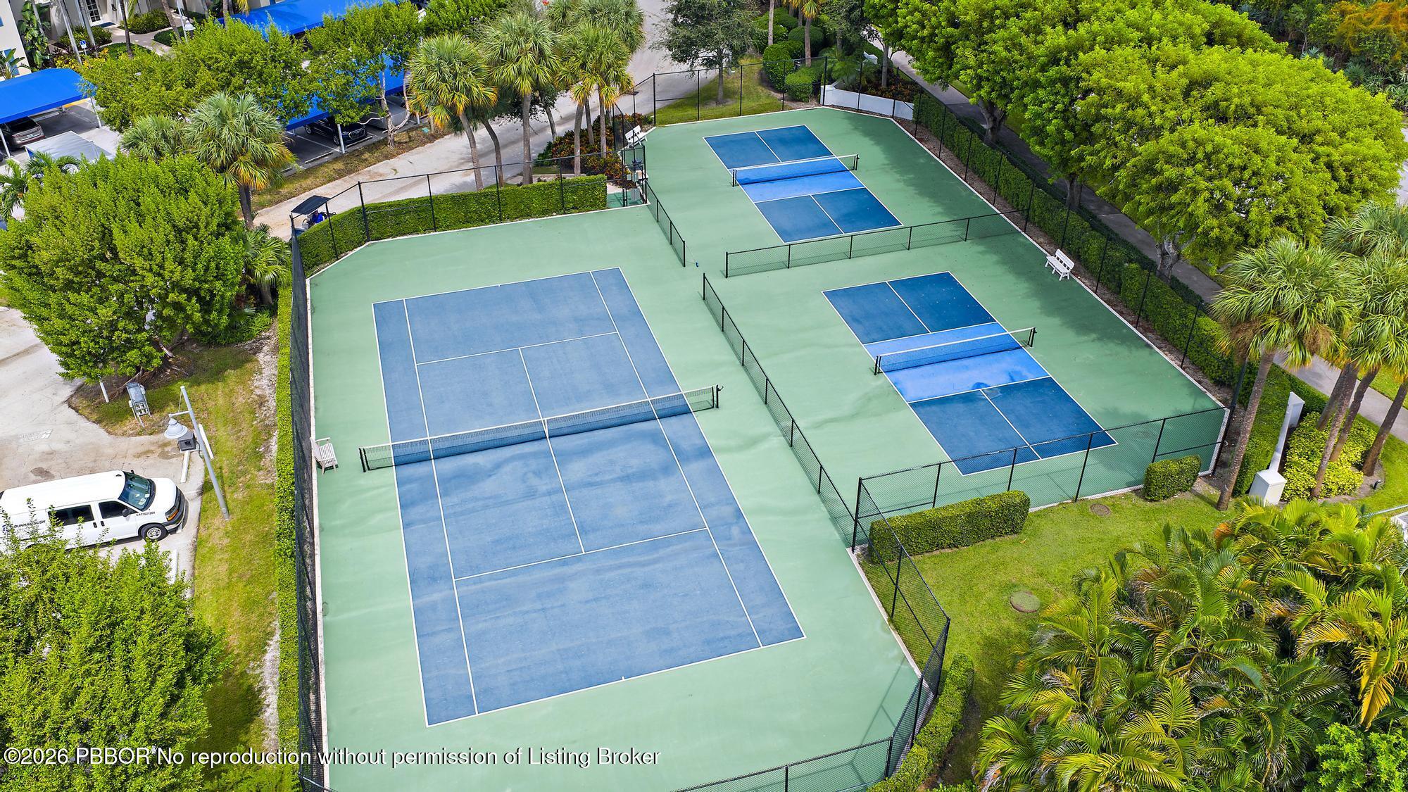 Aerial view of fenced tennis and pickleball courts surrounded by palms and greenery.
