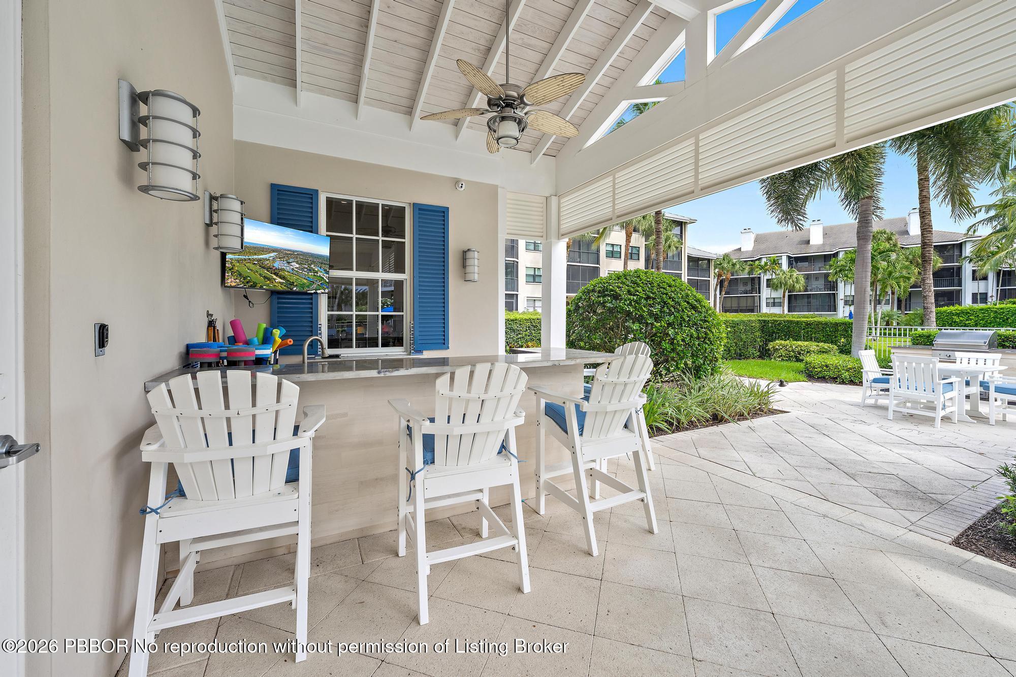 Covered patio with a bar, white Adirondack chairs, and a vaulted wood ceiling overlooking palms.