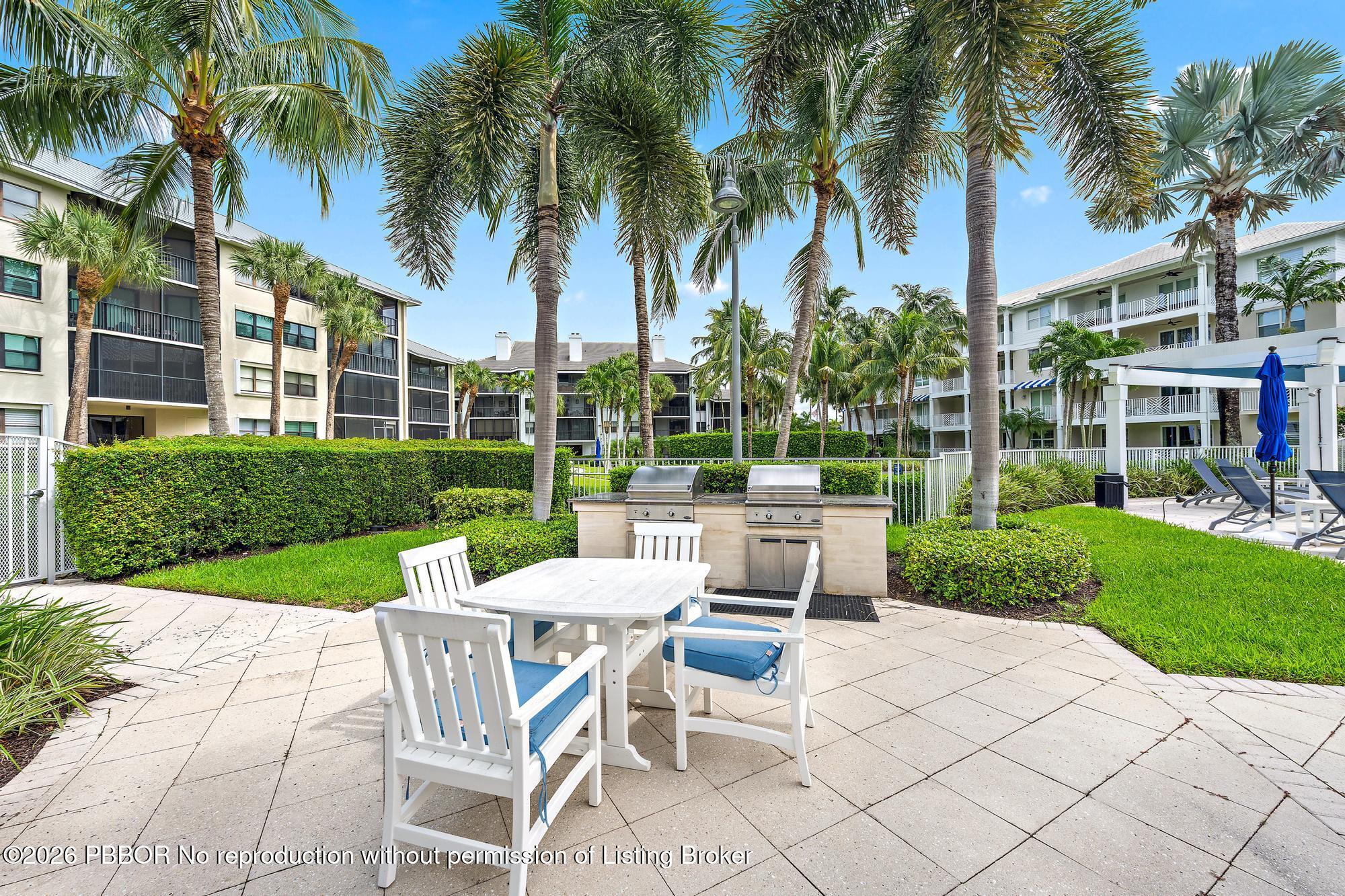 Condominium courtyard patio with outdoor dining, built-in grills, and tall palm trees.