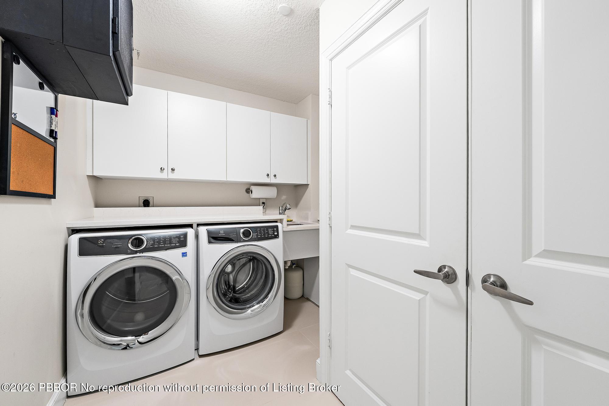 Laundry room with front-loading washer and dryer, white cabinets, and a small utility sink.