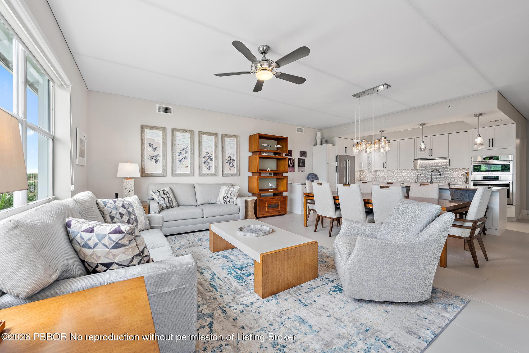 Open-plan living room and kitchen with floor-to-ceiling windows, gray seating, and a blue-patterned rug.