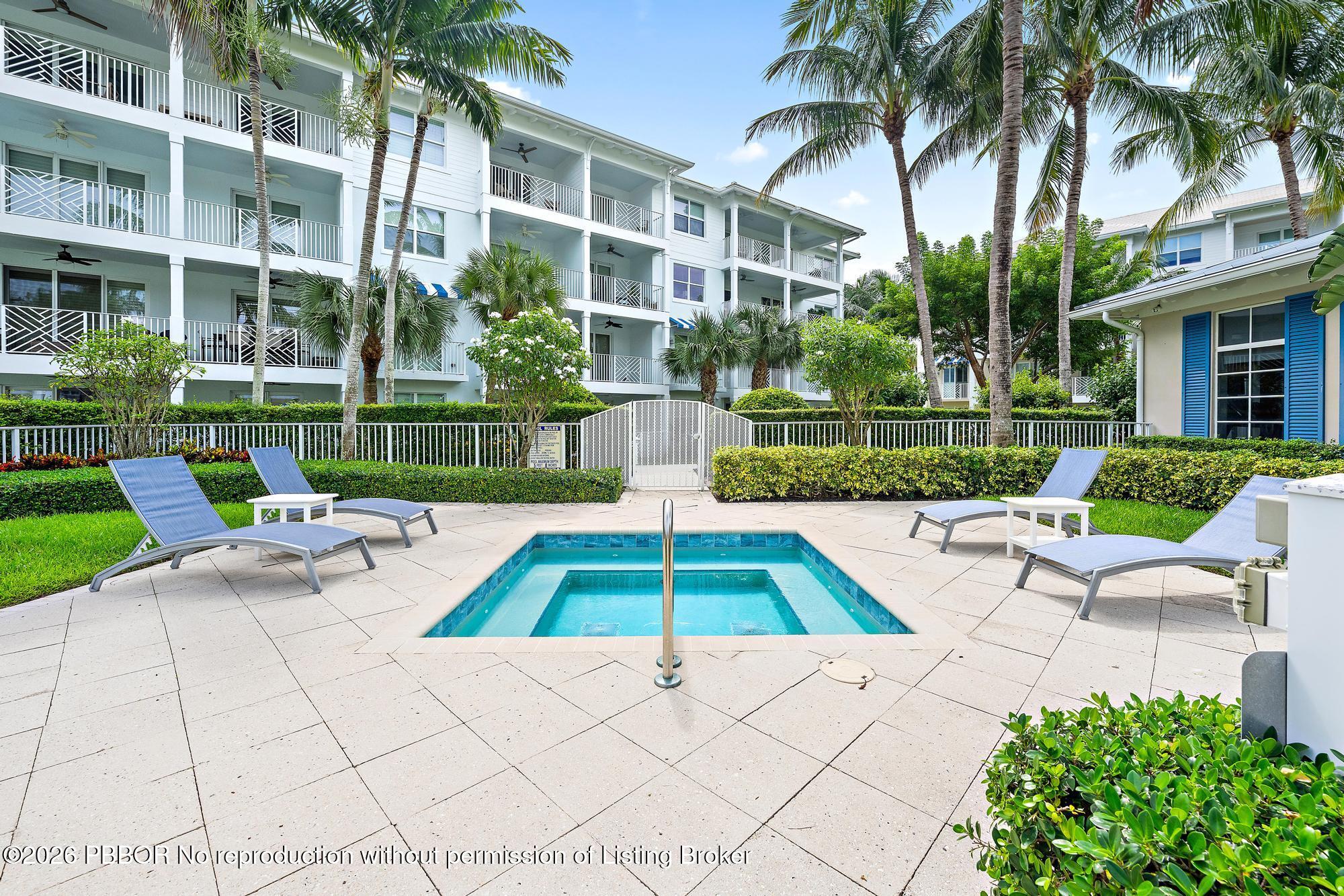 Outdoor pool courtyard with palm trees, lounge chairs, and a white condominium building.