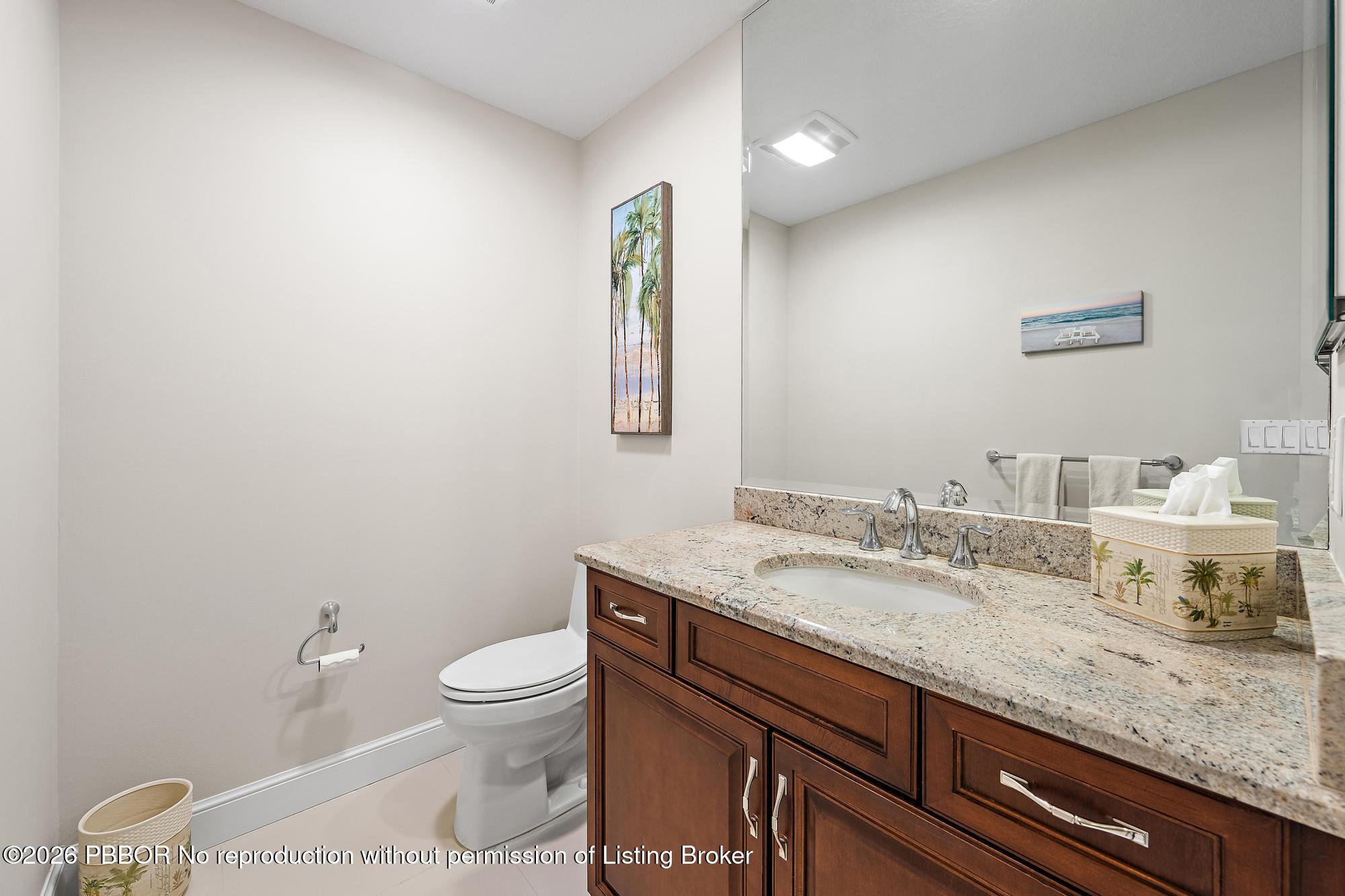 Bathroom with a dark wood vanity, granite countertop, large mirror, and toilet.