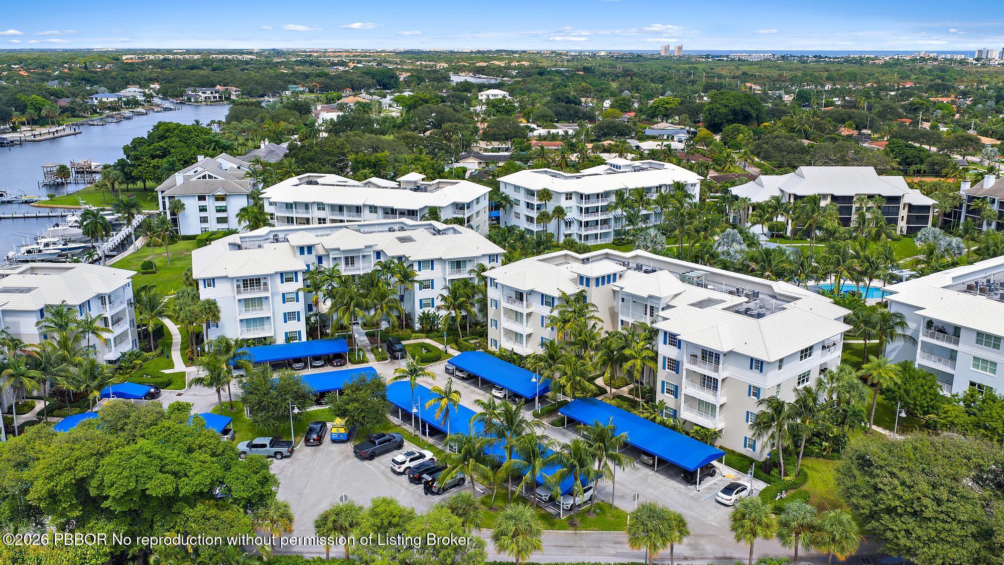 Aerial view of palm-lined condominiums beside a marina, with the ocean on the horizon.