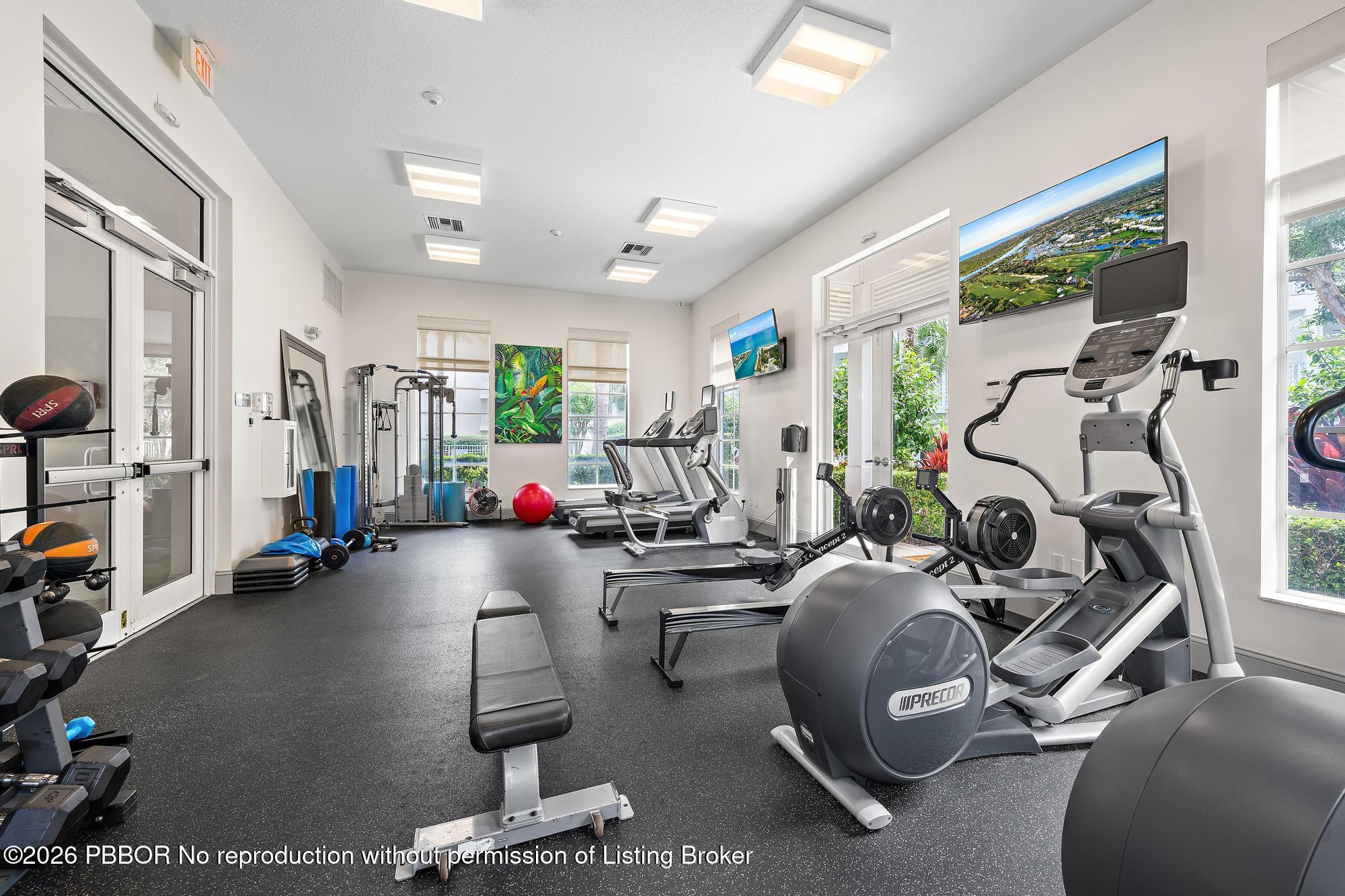 Fitness room with cardio machines, weight equipment, and large windows overlooking greenery.