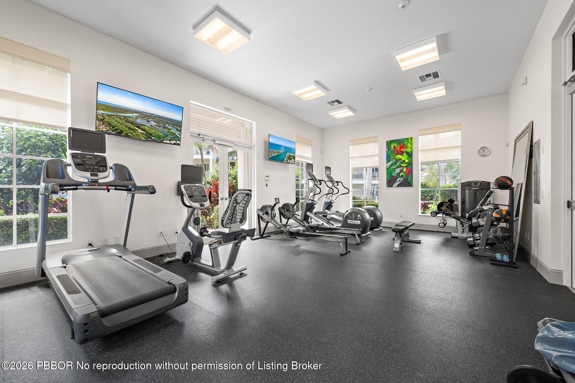 Fitness room with treadmills, bikes, and weight machines beside large windows.