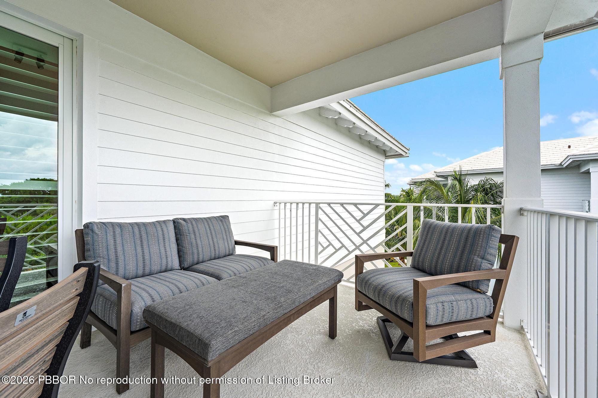 Covered balcony with gray outdoor seating, white railings, and palm trees beyond.