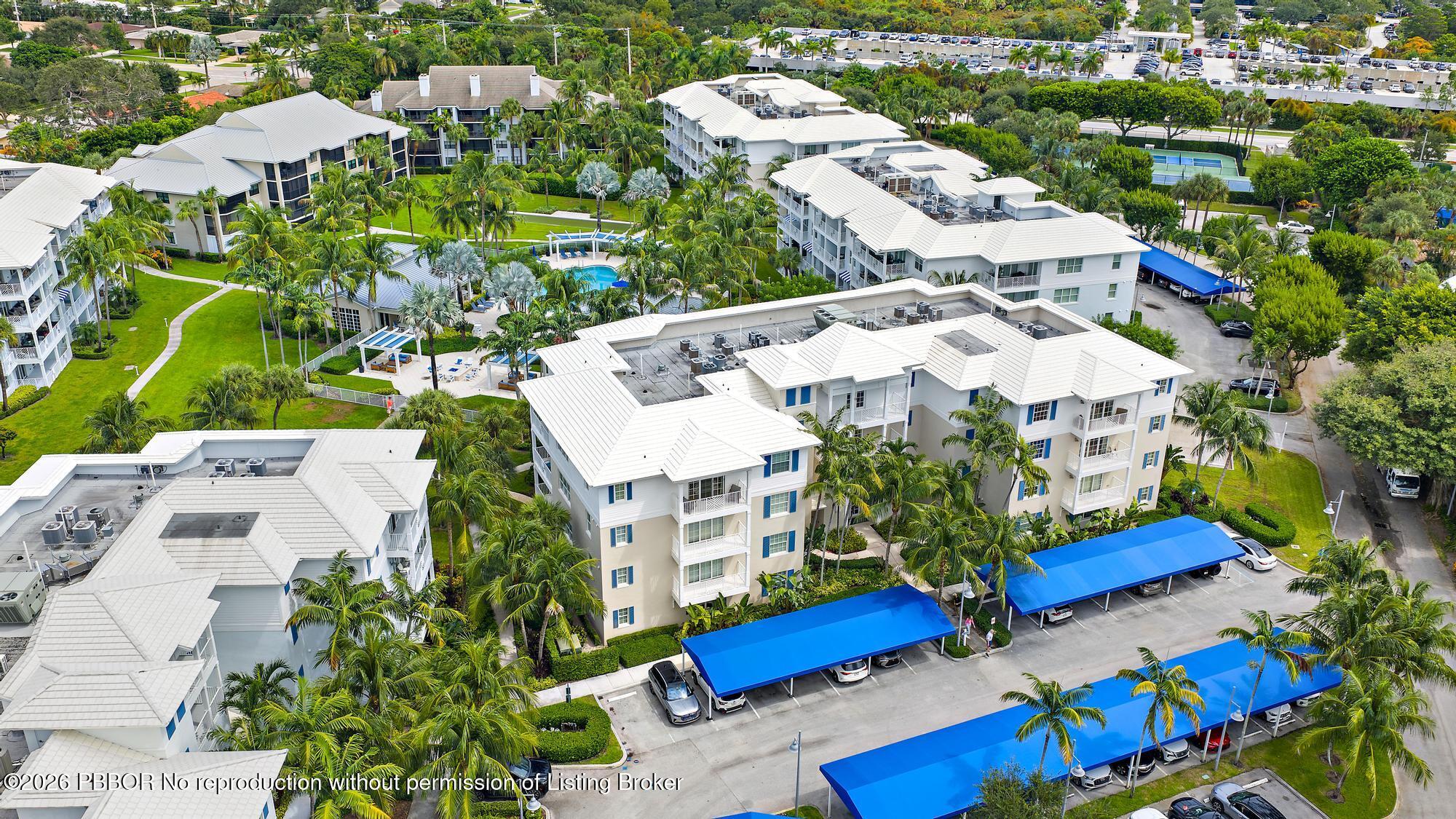 Aerial view of a tropical condominium community with a central pool and blue-covered parking.