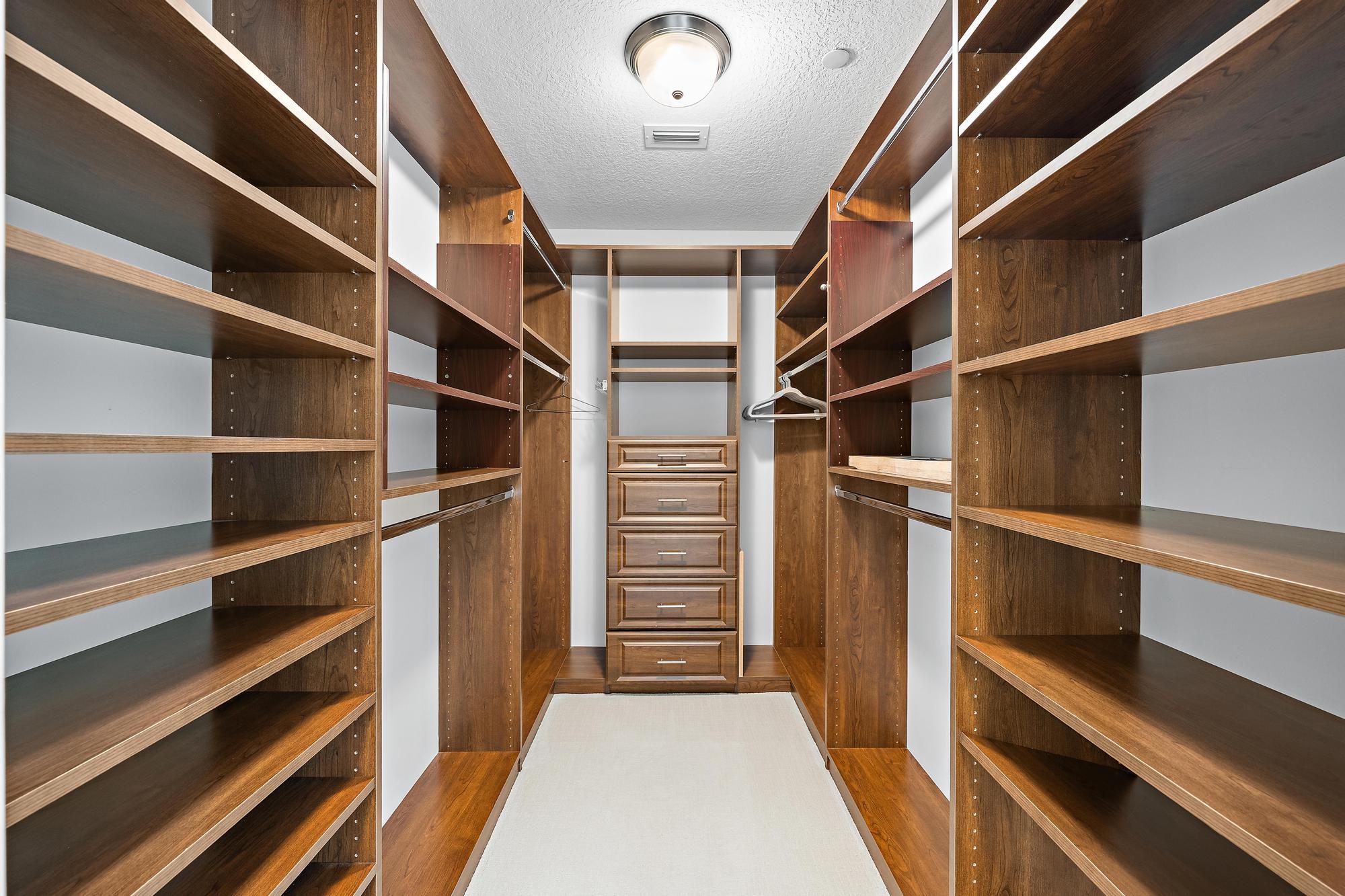Walk-in closet with built-in wood shelving, hanging rods, and central drawers.