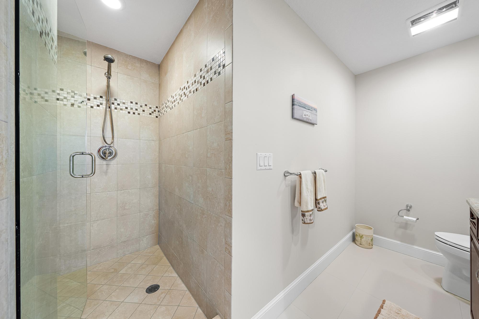Bathroom with a glass walk-in shower, beige tile, and mosaic accent band.