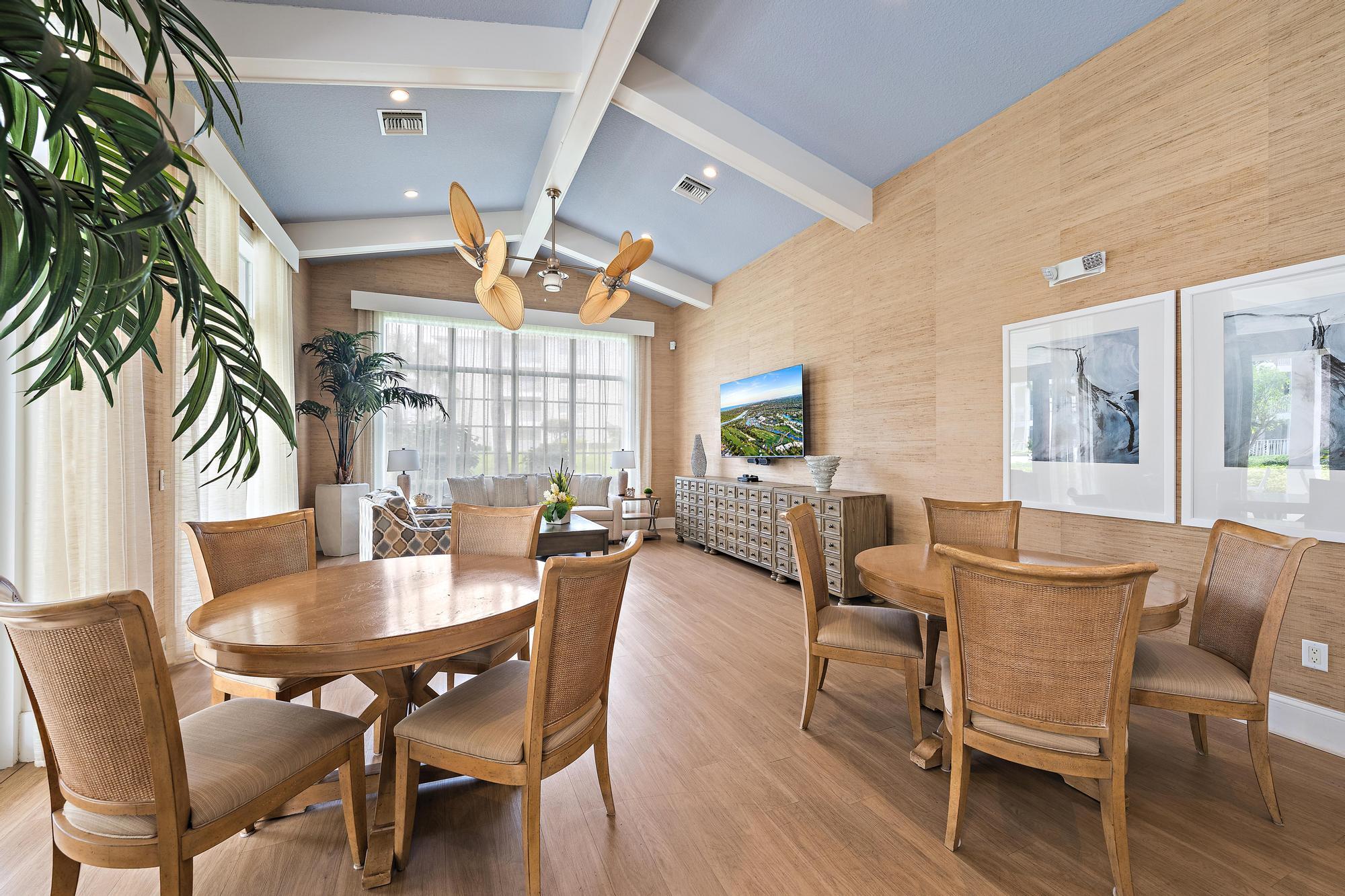 Open-plan dining and living room with round wooden tables, woven chairs, and a vaulted blue ceiling.
