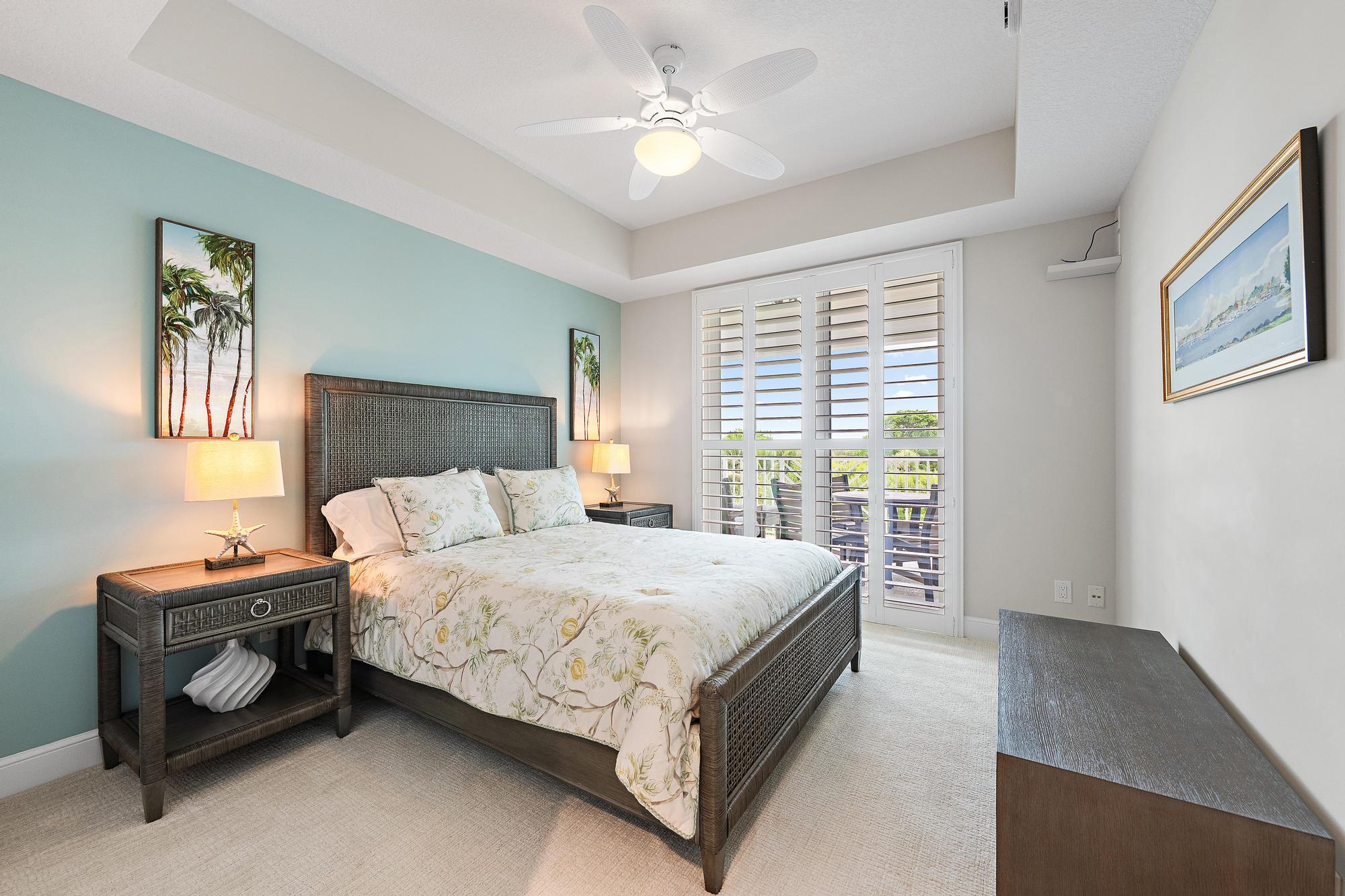 Bedroom with floral bedding, an aqua accent wall, and plantation shutters overlooking greenery.
