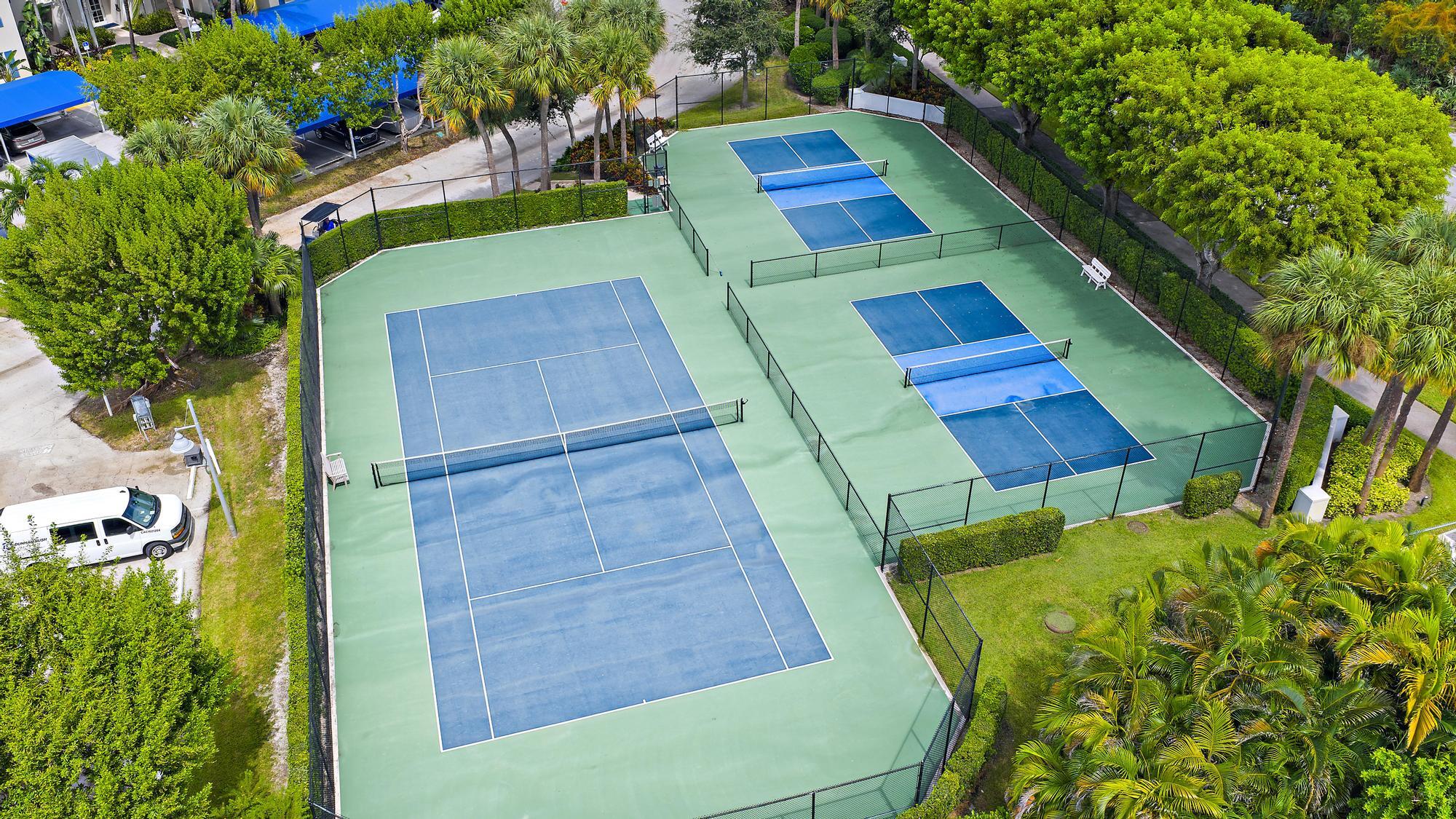 Fenced tennis and smaller courts surrounded by palm trees and greenery.