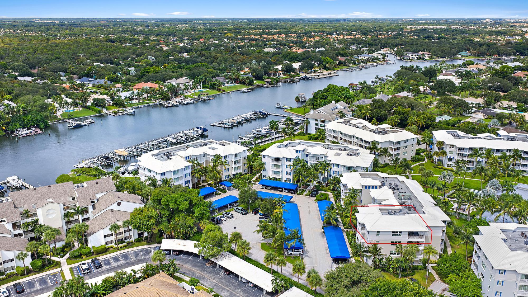 Aerial view of a waterfront condominium outlined in red beside a marina and broad waterway.