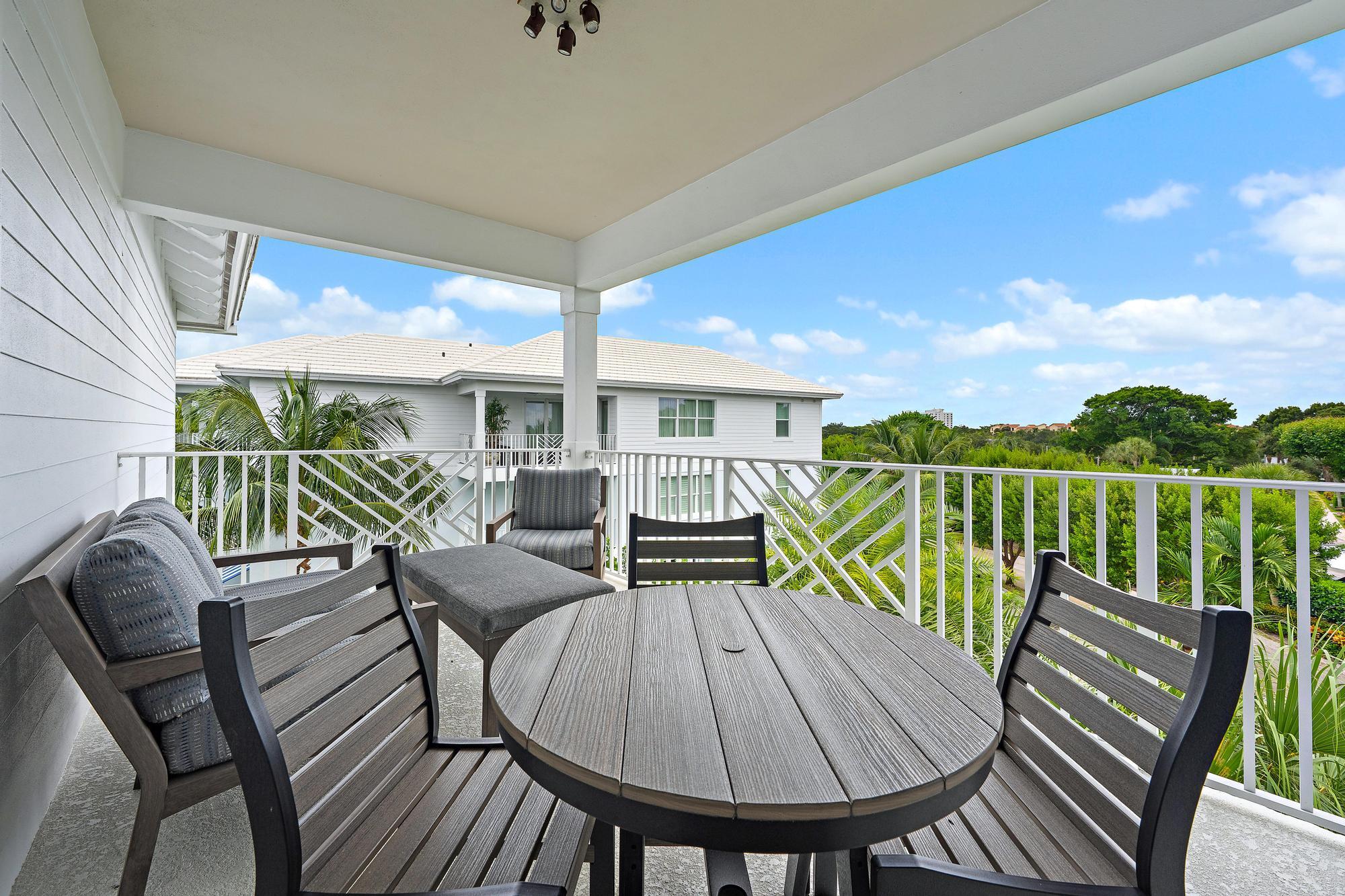 Covered balcony with a round dining table and gray chairs overlooking tropical greenery.