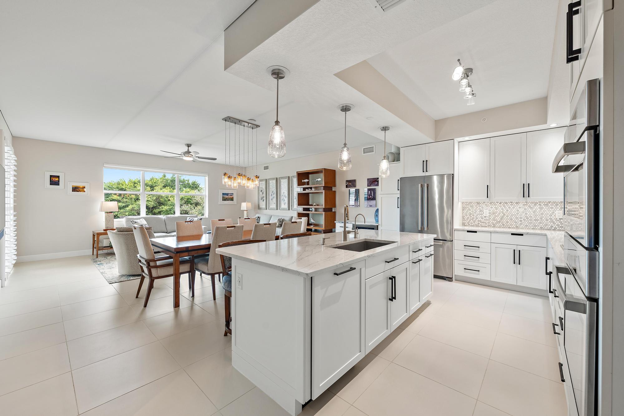 Open-plan kitchen with a large white island, stainless steel appliances, and adjoining dining area by wide windows.