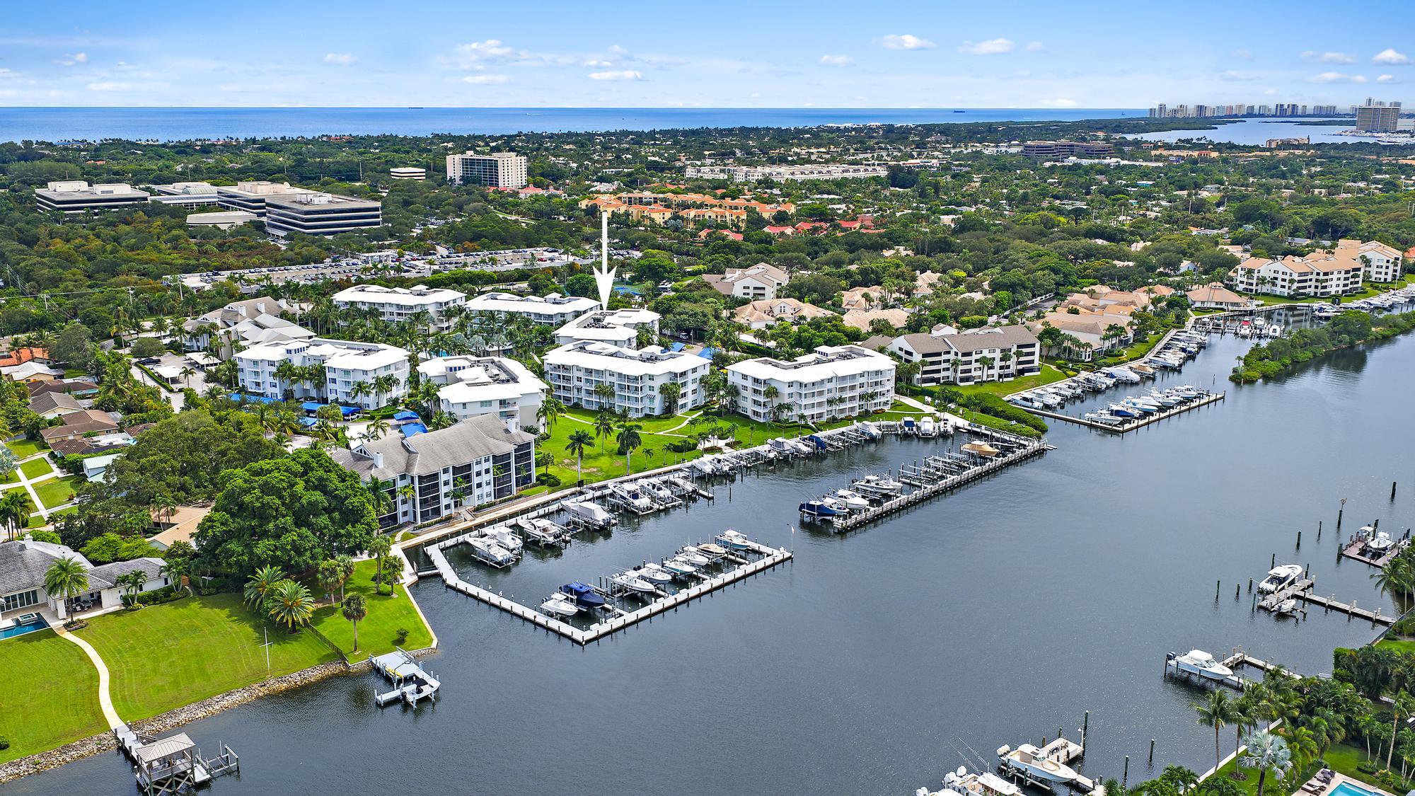 Aerial view of a waterfront condominium marked by an arrow, beside marina docks and the ocean.