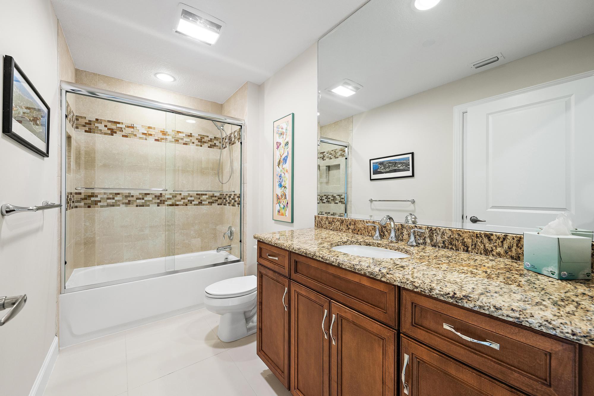 Bathroom with a glass-enclosed tub and shower beside a wood vanity with granite countertop.