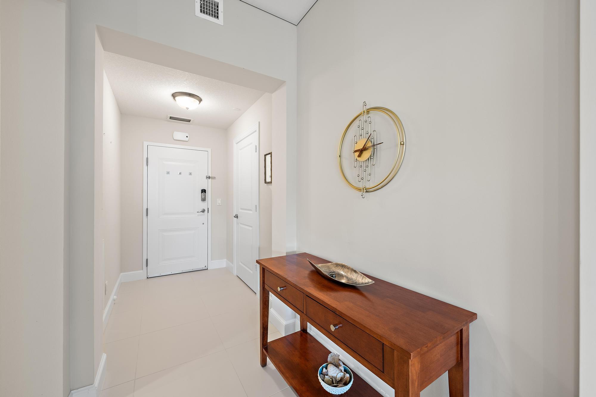 Entry foyer with a wooden console table, gold wall clock, and white front door.