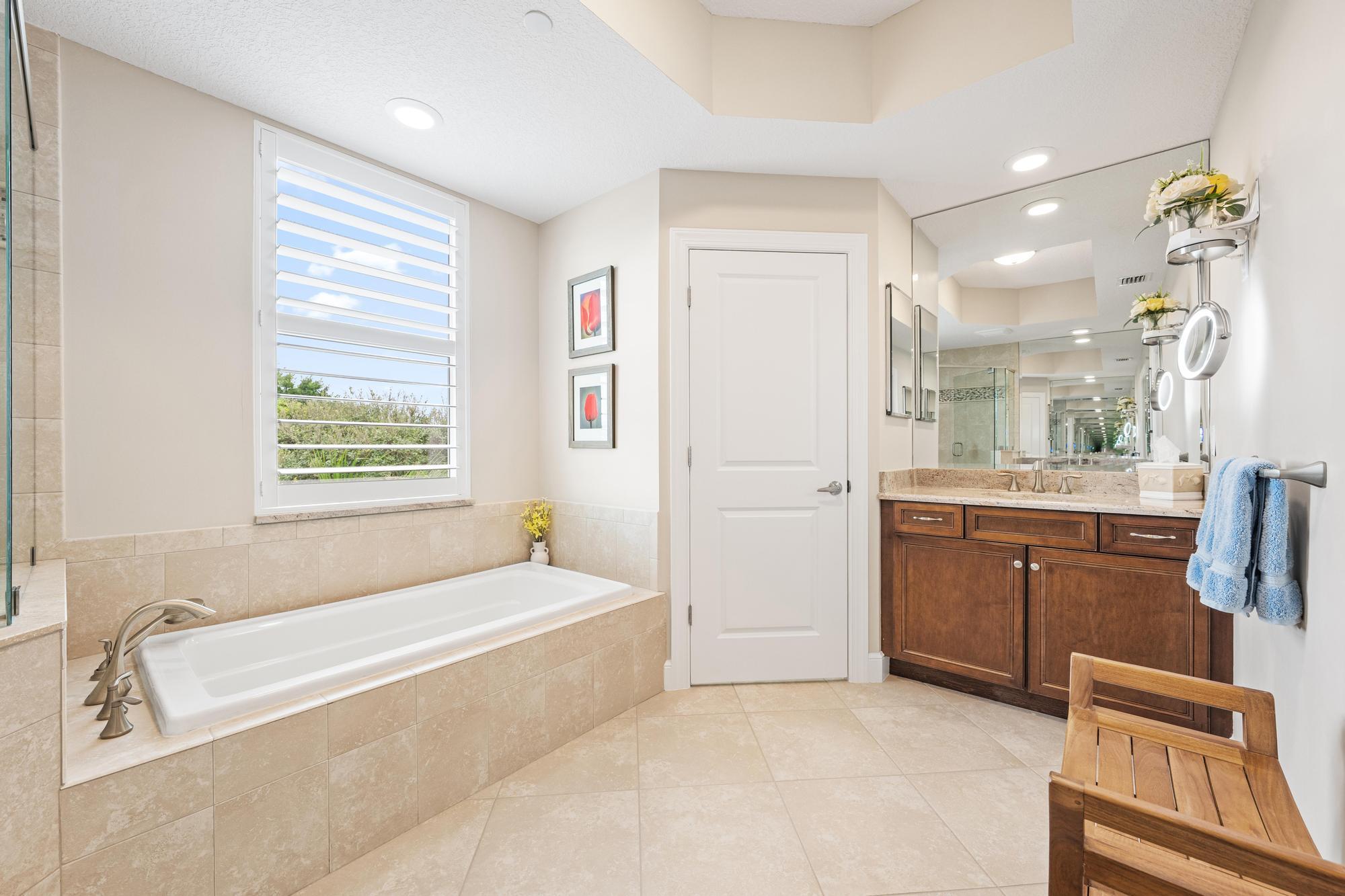 Bathroom with a built-in tub beneath a shuttered window and a dark wood double vanity.