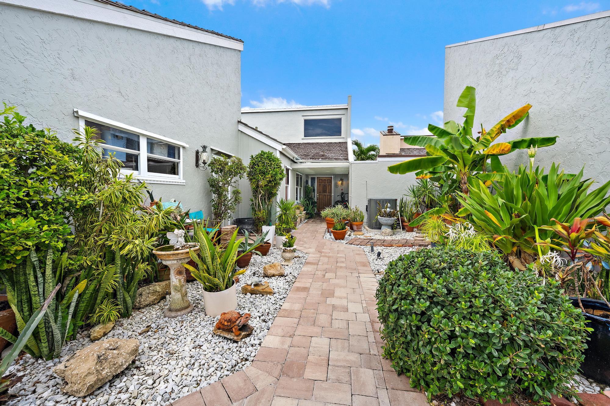 Home courtyard with a brick walkway, tropical plants, white gravel, and a small fountain.