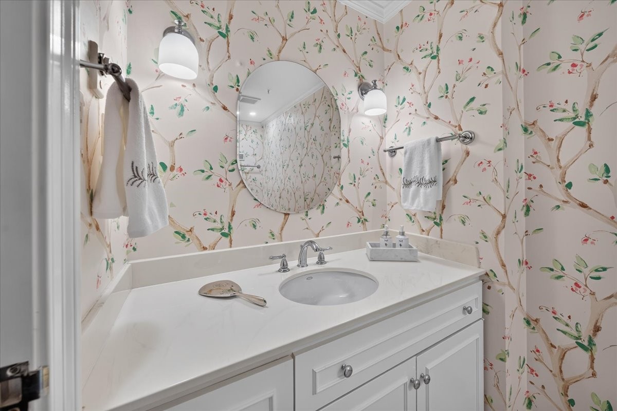 Bathroom vanity with a white sink, oval mirror, and floral branch-patterned wallpaper.