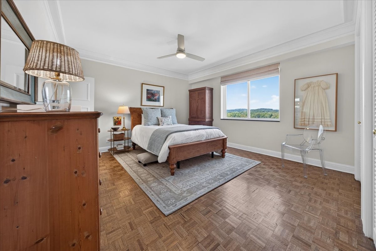 Staged bedroom with a wooden bed and parquet floor, looking out to green hills.
