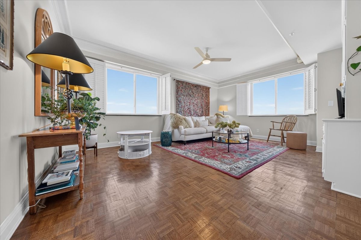 Furnished living room with parquet floors, a red patterned rug, and bright corner windows.