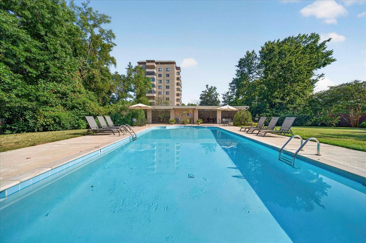 Outdoor swimming pool with lounge chairs and umbrellas, backed by a multistory residential building.