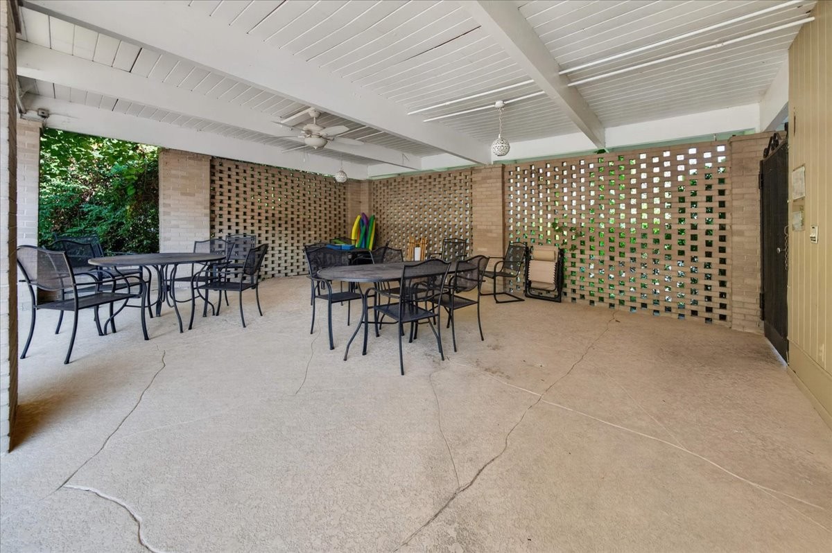 Covered patio with metal tables and chairs, brick lattice walls, and a white beamed ceiling.
